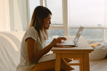 Woman in casual clothes working and typing with her computer laptop in her apartment in concept of work from home.