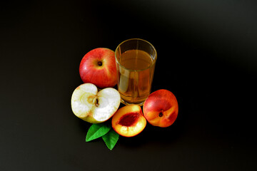 A glass of peach juice with an apple on a black background, next to pieces of ripe fruit.