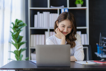 Cheerful Asian woman working with laptop in office, happy in formal suit working in office Charming...