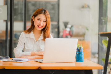 Obraz na płótnie Canvas Cheerful Asian woman working with laptop in office, happy in formal suit working in office Charming smiling female office worker, financial accounting concept