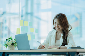 Cheerful Asian woman working with laptop in office, happy in formal suit working in office Charming...