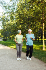 Senior mature couple running together in the park looking at each other while jogging slimming exercises.