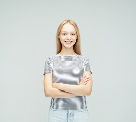 smiling blond woman wearing stripes t-shirt with crossed arms over light grey background.