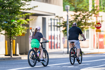 Father and daughter ride bicycles along a dedicated bike path along the street of a modern city