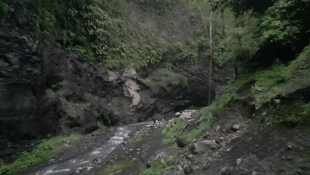 Low aerial flies up hazy steep narrow jungle canyon on Java, Indonesia