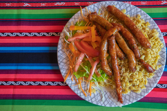 traditional Bolivian food, "chorizos de Tarata", plate with wheat and vegetable salad, on a "aguayo" tablecloth