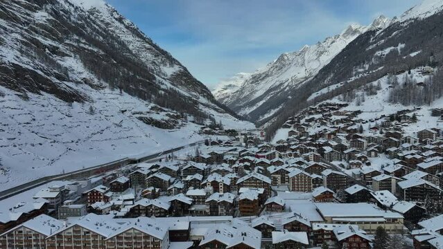 Tall mountain peaks and valley in Zermatt, Switzerland with ski resort and town on bright winter day. Aerial Drone.