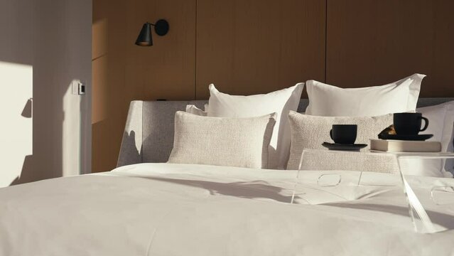 a luxury bedroom with a large white king bed and a bed side table on it which includes 2 black coffee mugs and a book