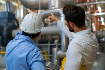 Professional male electrical engineer in safety uniform working and discussion at factory site control room. Industrial technician worker maintenance power system at manufacturing industry plant room.