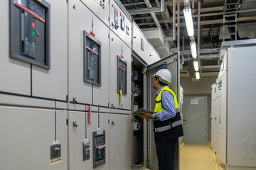 Asian mature man engineer in safety uniform working on tablet in factory server electric control panel room. Industrial technician worker maintenance checking power system at manufacturing plant room.