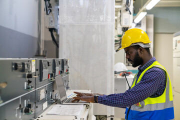 Industry factory manufacturing concept. African man engineer working on laptop computer in electric server control panel room. Industrial technician worker maintenance check power system in plant room