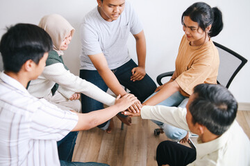 Obraz premium People sitting in circle and putting hands together in community meeting or group therapy session.
