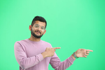 A man, on a green background, in close-up, points to the side