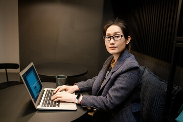 A portrait of a professional investment adviser Asian woman was sitting in front of the desk in front of the laptop, watching the camera and smiling.