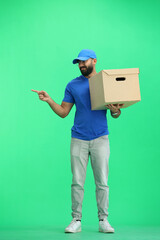 A male deliveryman, on a green background, full-length, with a box, points to the side