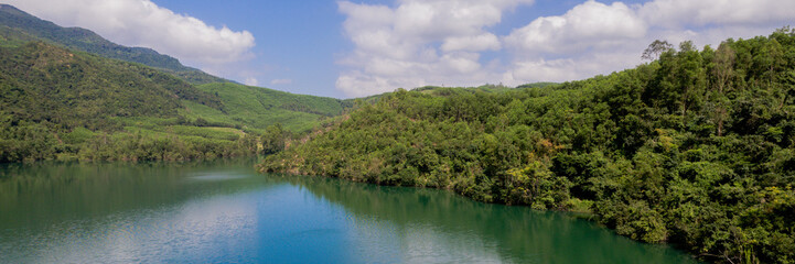 Fototapeta premium Tranquil forested hills surrounding a calm lake under a partly cloudy sky, depicting serene natural beauty, Earth hour concept