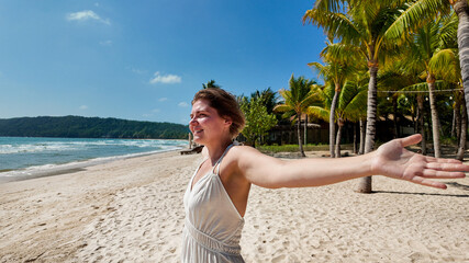 Woman in a white dress with arms wide open, enjoying the freedom and serenity of a tropical beach...
