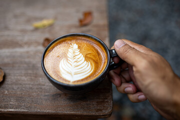 Hand holding a coffee cup placed on a wooden table with warm tones in the morning