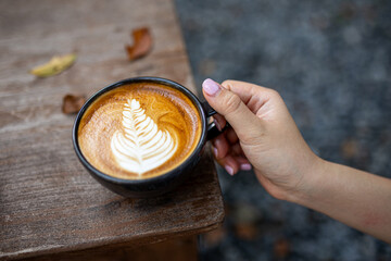 Hand holding a coffee cup placed on a wooden table with warm tones in the morning