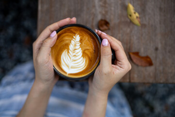 Hands holding a coffee cup placed on a wooden table with warm tones in the morning