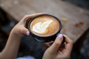Hands holding a coffee cup placed on a wooden table with warm tones in the morning