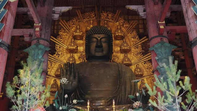 Giant Buddha statue in Tōdai-ji temple, Nara, with intricate gold patterns in background, candles and offerings in front