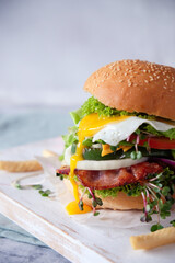 Cheeseburger with fried melting egg, bacon, lettuce and tomato