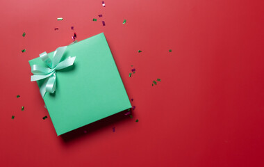Green gift box wrapped and ribbon on red background.