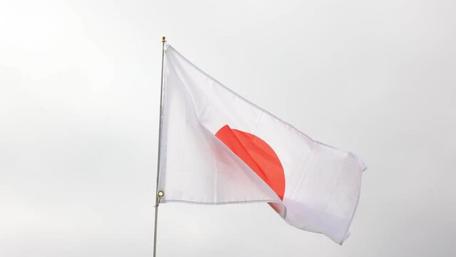 Large flag of Japan fixed on metal stick waving against background of cloudy sky during daytime 