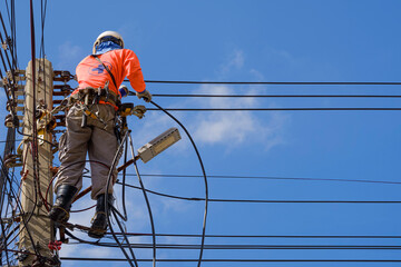 Electrician with Safety equipment and various work tools is Installing Cable lines and Electrical system on Electric Power Pole against blue sky background, Bottom view with copy space