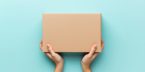 Top view to female hand holding brown cardboard box on light blue background. Mockup parcel box. Packaging, shopping, delivery concept