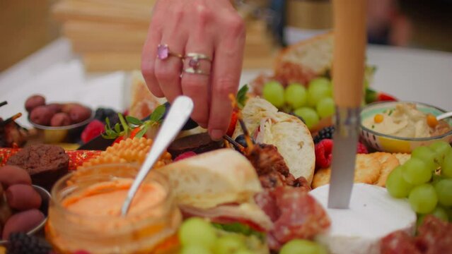 Caucasian female hand picking up mini kebab from food board outside during the day charcuterie
