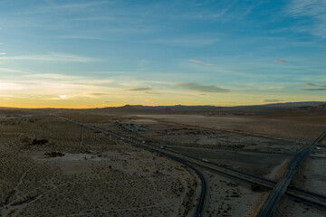 an aerial shot of majestic mountain ranges in the desert at sunset with cars and trucks driving on the highway in Yermo California USA