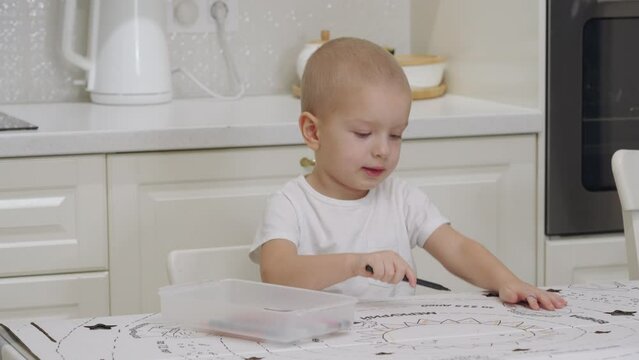 3-year-old child drawing with felt tip pens on large sheet of cardboard. Cute little boy drawing at home.