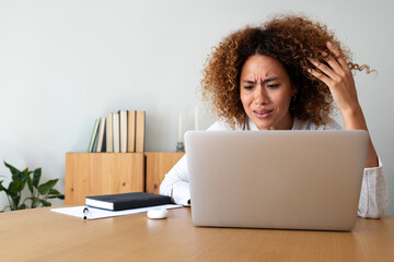 Multiracial hispanic woman feeling angry and frustrated while working with laptop at home office....
