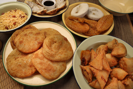 Bengali sweet savoury snacks variety stuffed pancake chitoi bhapa nakshi pakkon pitha singara samosa dal aloo puri fried flattened rice cheera mix on enamel tin metal plate over rustic background