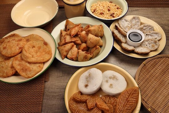 Bengali sweet savoury snacks variety stuffed pancake chitoi bhapa nakshi pakkon pitha singara samosa dal aloo puri fried flattened rice cheera mix on enamel tin metal plate over rustic background