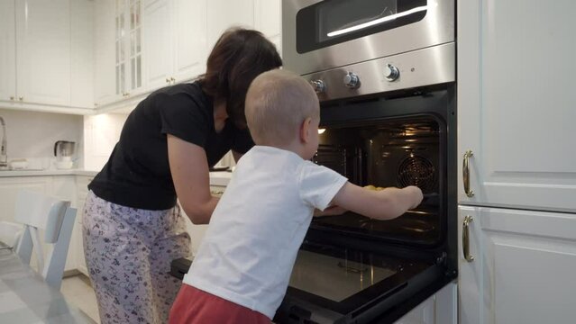 little boy helping mom cooking baked jacket potatoes at home, mother with child preparing dinner together in modern kitchen