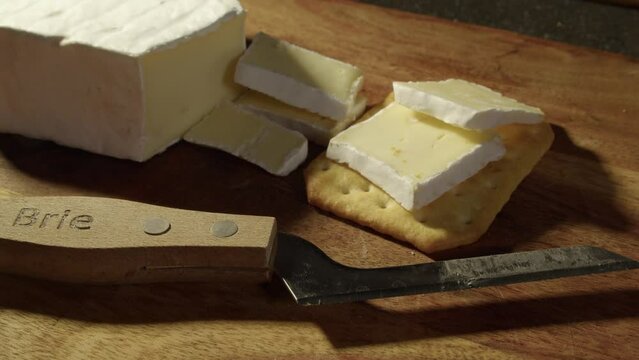 Close up slices of Brie cheese put onto soda cracker, knife on board