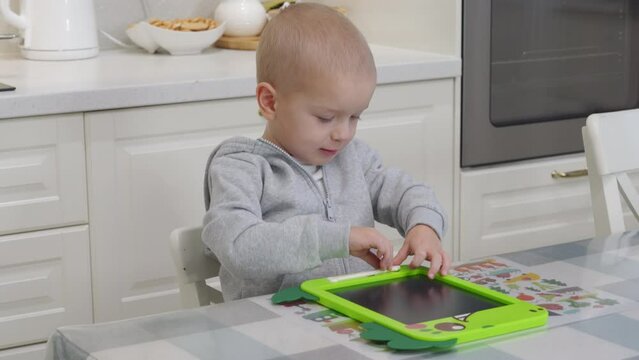 3-year-old child drawing with pen on electronic drawing writing board. Little boy playing with drawing tablet for kids.