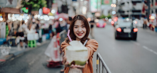 Young asian woman traveller standing and drinking coconut water. Beauty traveller female in city lifestyle chinatown street food market Bangkok, Thailand