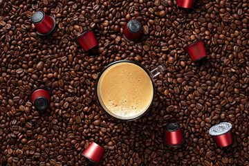 Top view of many roasted coffee beans and glass cup with fresh espresso coffee. Capsules for coffee...