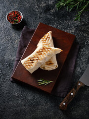 Top view of a beautiful wooden cutting board with shawarma. On a dark marble background. Red, black pepper, knife and rosemary.