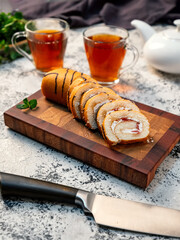 Vertical image of a sponge roll sliced on a beautiful wooden board on a background of glass cups with tea. Delicious dessert for breakfast..