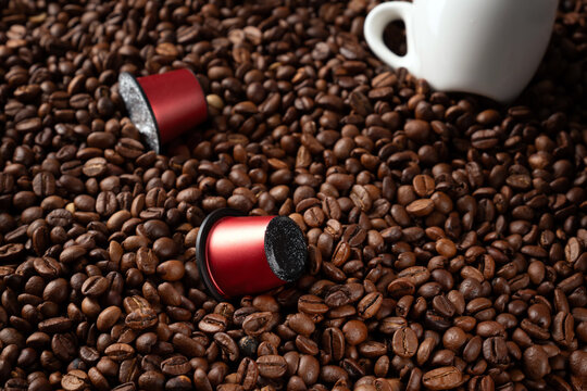 Close-up of many roasted coffee beans and red capsules for coffee machines. Conceptual image.