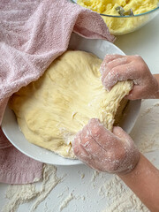 The hands of child knead the dough for making pies on white table, top view.