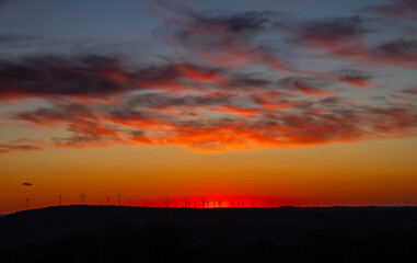 Fototapeta premium A sunset over the Australian countryside with a silhouette wind farm spread across the horizon and orange clouds in the sky near Glenn Innes in New South Wales, Australia.