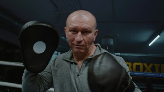 POV of professional trainer with punching mitts on hands taking punches from boxer. Coach trains fighter on boxing ring before competition. Physical activity and intense workout. First person shooting
