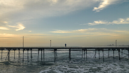 Lonely man standing on a pier at sunset. Feeling of peace or sadness.