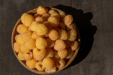 Yellow raspberries in a wooden bowl on the table. Summer berries background. Vitamin food, berry harvest. Healthy nutrition.